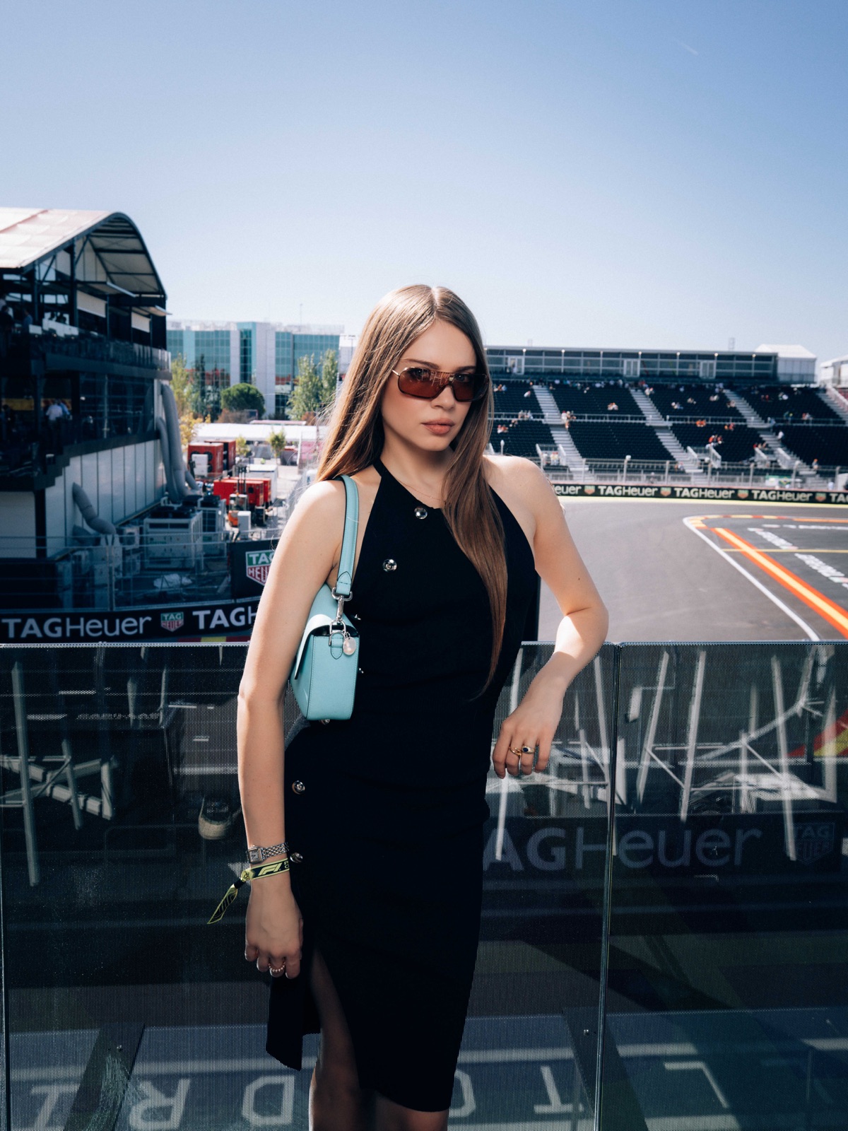 Xenia Tchoumi on a Paddock Club terrace above the Madring circuit at the Formula 1 Spanish Grand Prix 2026 in Madrid, in sunglasses and a black dress with a Fendi x Tiffany Baguette