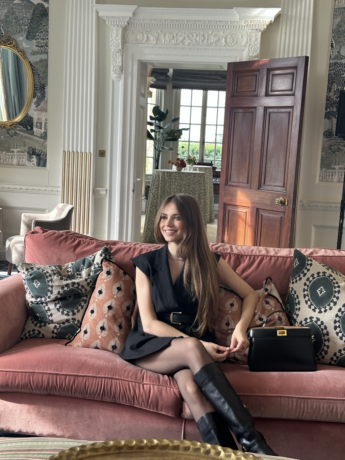 Xenia Tchoumi on a rose velvet sofa in a salon of Hedsor House, her black Fendi bag beside her, at The Hedsor Hundred