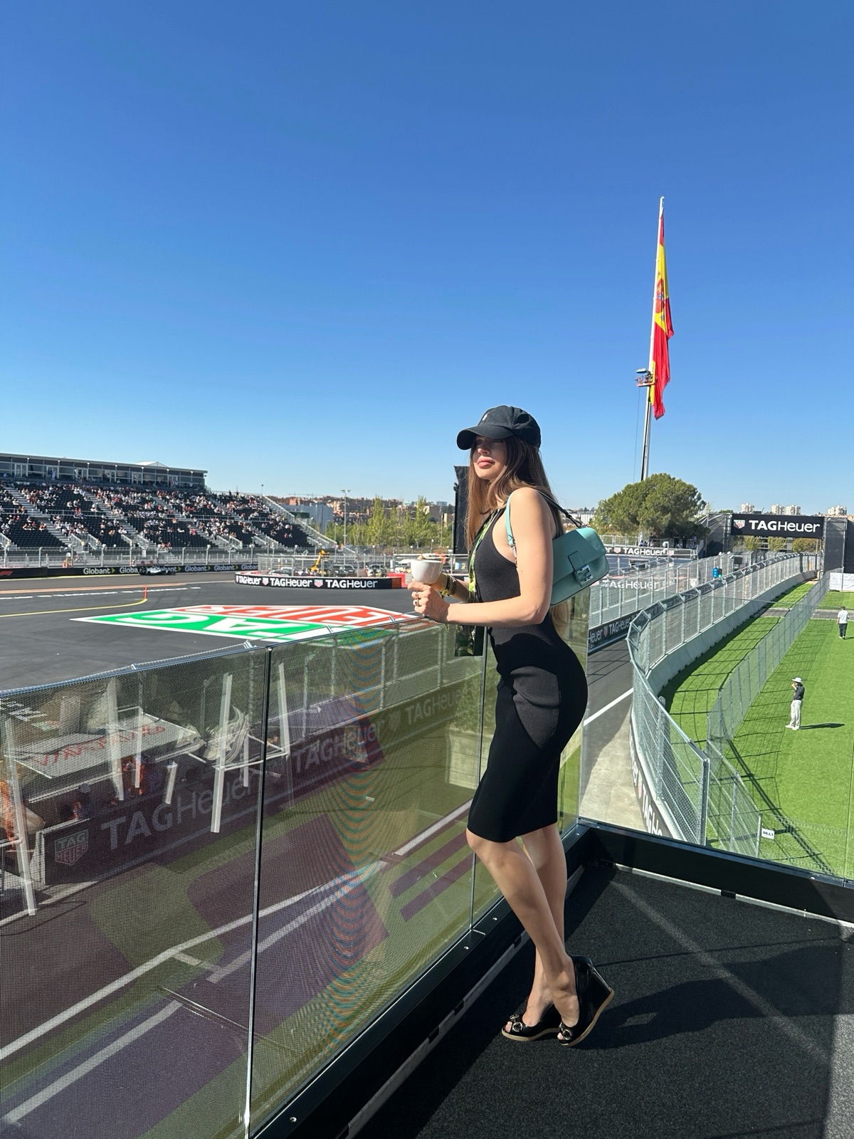 Xenia Tchoumi in a black cap overlooking the Madring track and the Spanish flag at the Madrid Grand Prix 2026, carrying the Fendi x Tiffany Baguette
